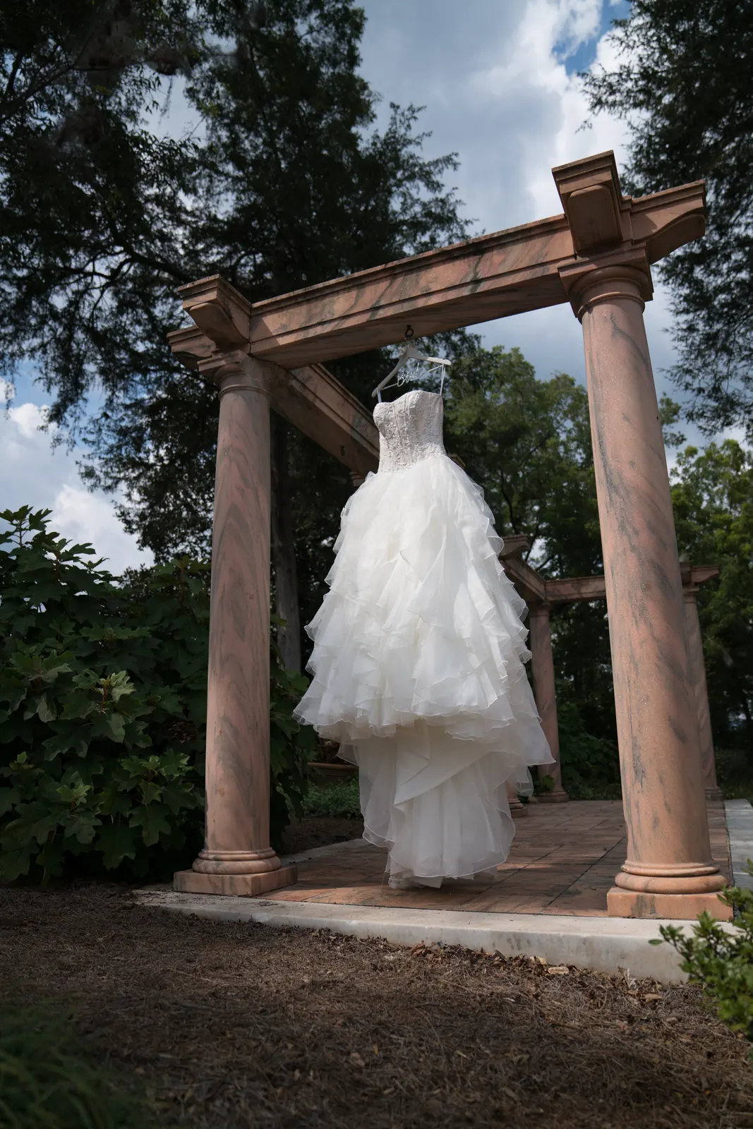Feathered wedding gown hanging between stone columns in a garden